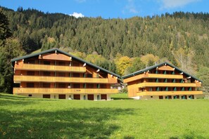 A wooden chalet-style building with multiple balconies, situated in a grassy area with a forested mountain backdrop. - Apartment for 4 people in Chatel (Châtel)