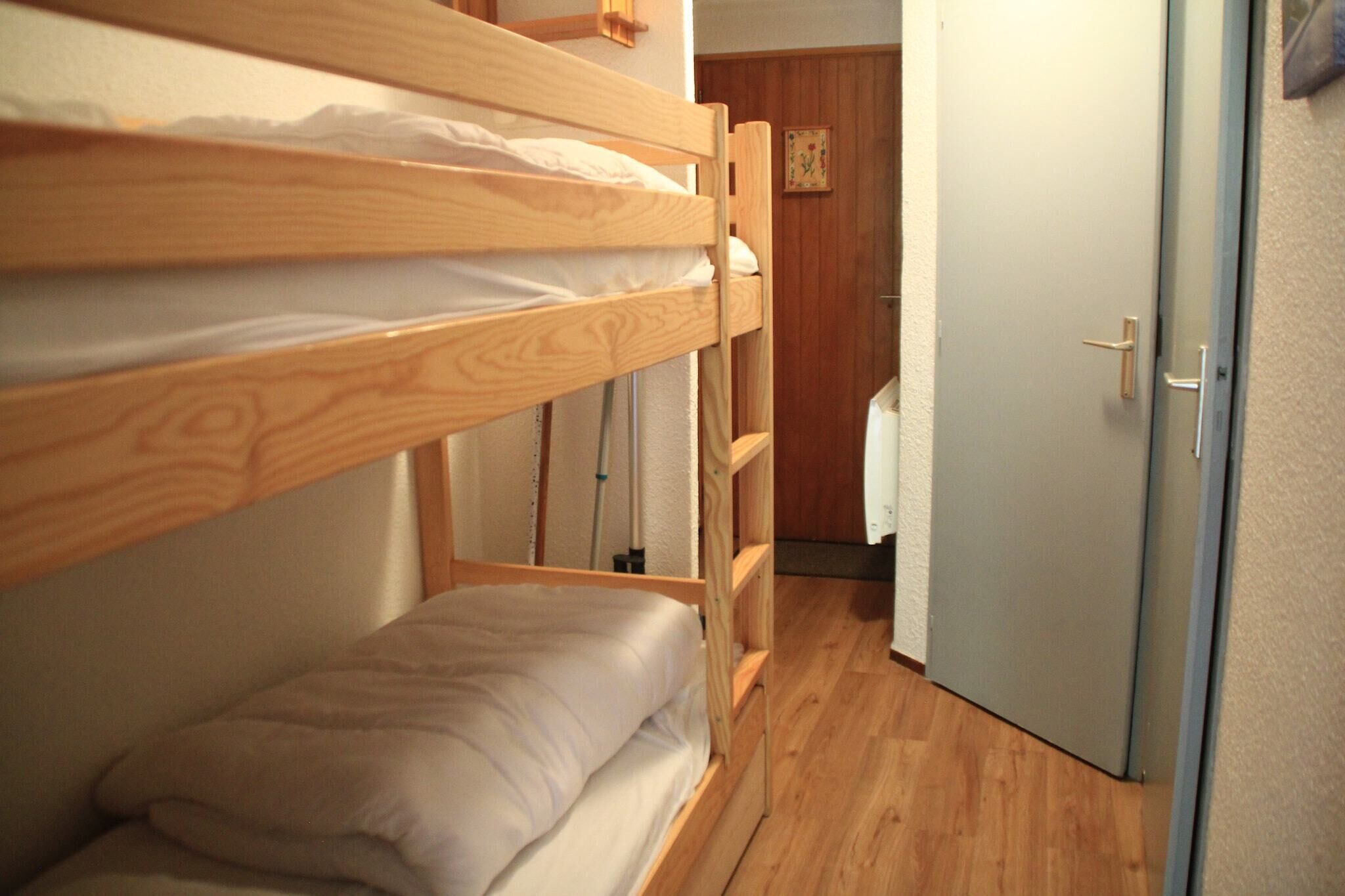A bunk bed room with a wooden floor, a door, and a small wall-mounted shelf.