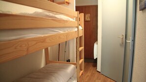 Ein Schlafzimmer mit Etagenbetten, Holzboden, einer Tür und einem kleinen Wandregal.