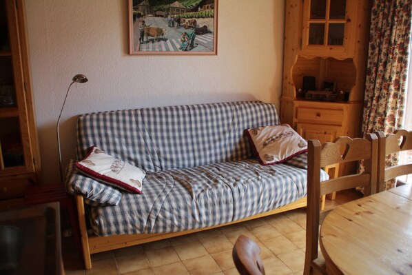 Een gestreepte bank met kussens, een houten kast en een eettafel in een kamer met een betegelde vloer.