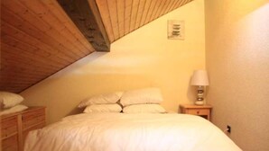 Une chambre avec un plafond en pente, un lit avec une literie blanche, une table de chevet avec une lampe et une petite œuvre d’art accrochée au mur.