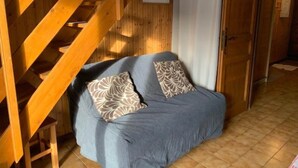 Une pièce chaleureuse avec un escalier en bois, un canapé bleu orné de coussins à motifs et un sol carrelé.