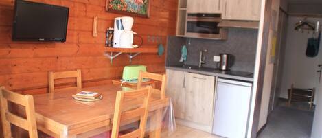 A wooden dining table with chairs, a coffee maker, and a television on the wall.