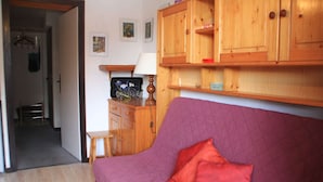 A room with a purple sofa, wooden cabinets, a small table with a lamp, and a television on a wooden stand. - Studio in Portes du Soleil near Gondola (Châtel)
