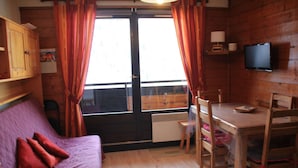 A cozy room with a purple sofa, wooden table, and chairs, a television, and a window with curtains. - Studio in Portes du Soleil near Gondola (Châtel)
