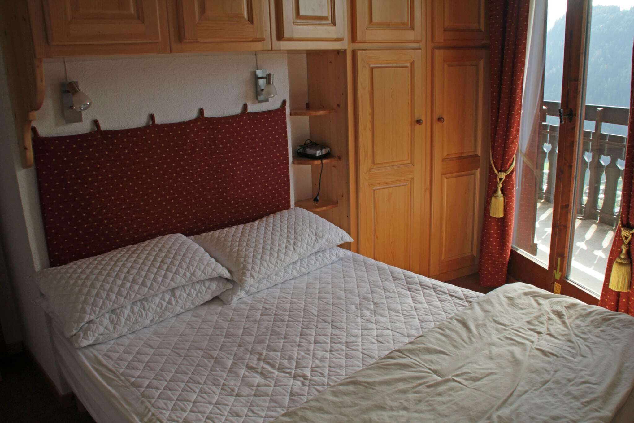 A bedroom with a bed, wooden cabinets, and a window with curtains.