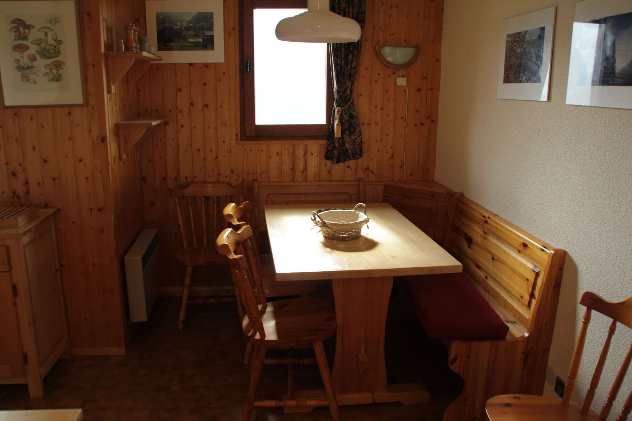 Un intérieur en bois comprenant une table à manger, des chaises, un banc, un radiateur et des tableaux encadrés accrochés aux murs.