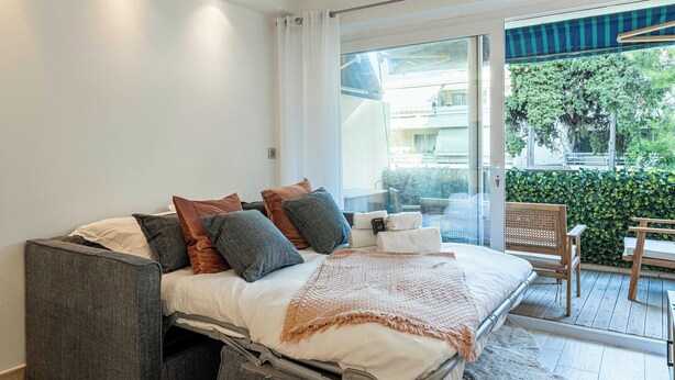 Une chambre moderne avec un lit, des oreillers, une table de chevet et une vue sur un balcon avec une chaise.
