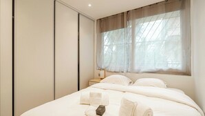 Une chambre d’hôtel comprenant un lit, une table de chevet, une fenêtre avec des rideaux légers et une armoire.