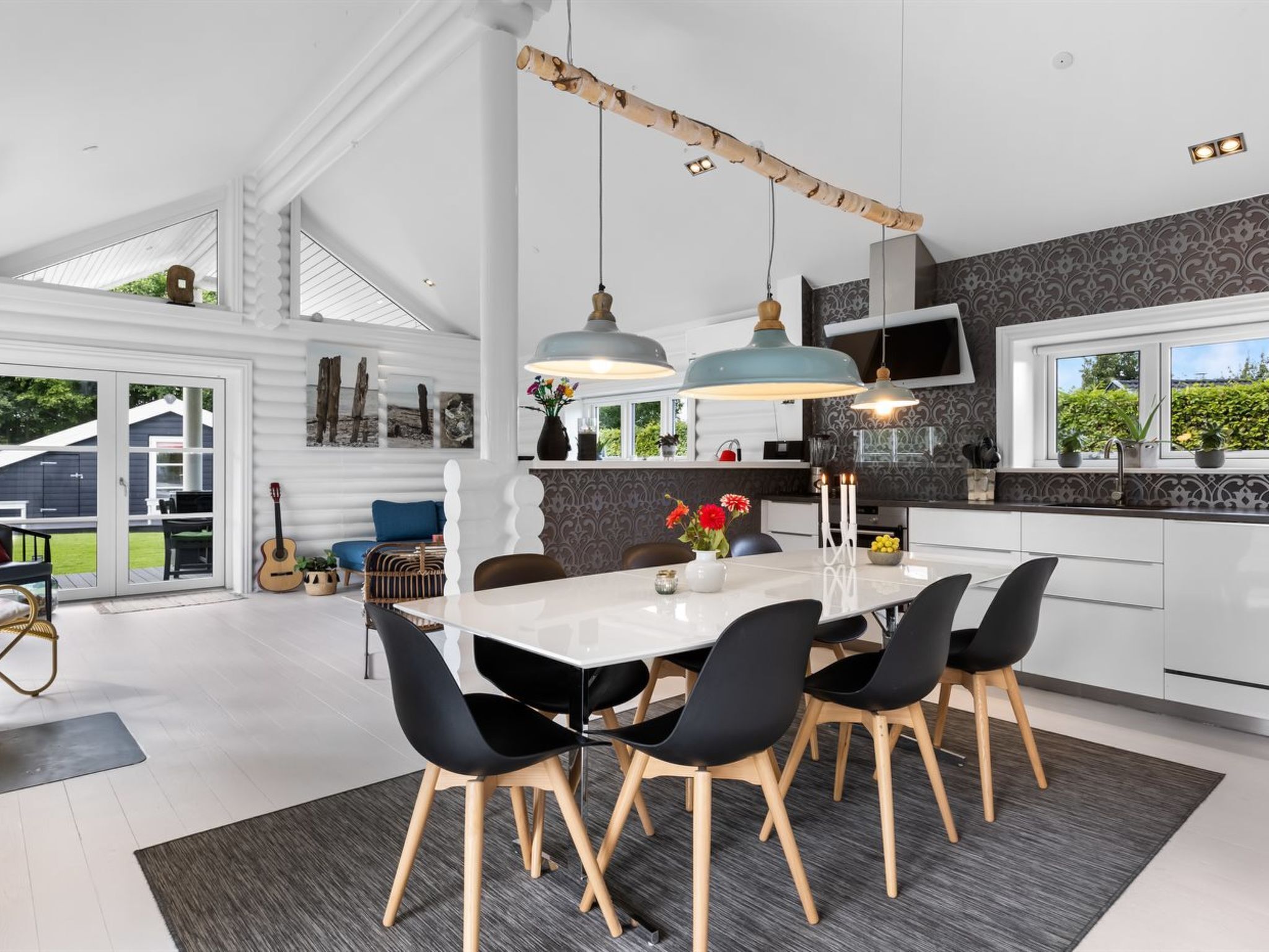 Une cuisine moderne avec une grande table à manger, des chaises noires et des luminaires suspendus.