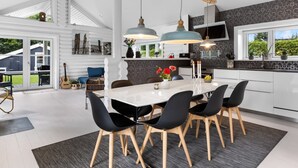 Een moderne keuken met een grote eettafel, zwarte stoelen en hanglampen.