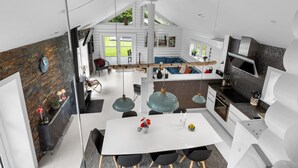 Een moderne keuken met een centraal eiland, een eethoek met een witte tafel en een gezellige zithoek met een open haard.