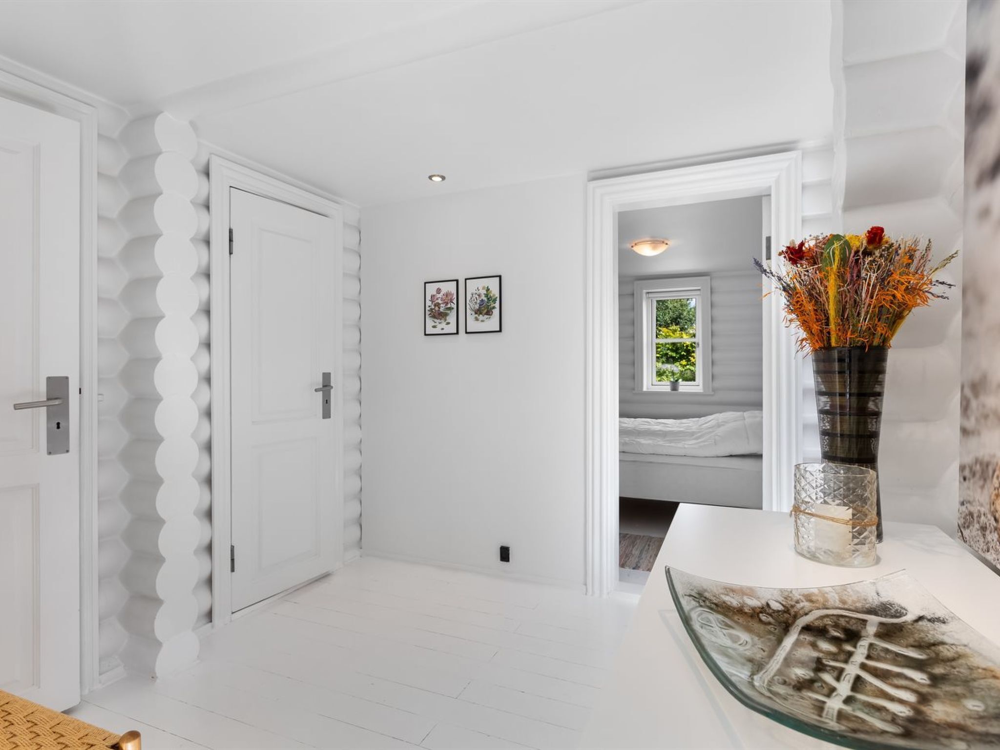 Un pasillo con puertas blancas, una obra de arte enmarcada y un florero con flores sobre una mesa.