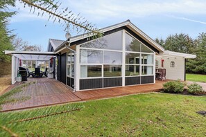 Une maison moderne dotée d’une grande baie vitrée, d’une terrasse en bois et d’un petit jardin.
