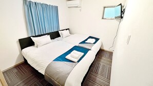 Een hotelkamer met een groot bed, een aan de muur bevestigde televisie en een raam met gordijnen.