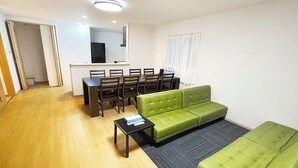 Een moderne woonkamer met een groene bank, een eettafel met stoelen en een kleine salontafel.