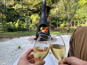 Two people holding wine glasses in a garden with a fire pit in the background.