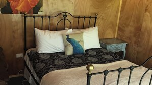 A wooden-paneled room with a bed featuring a metal frame, a wall-mounted light fixture, and a painting above the bed.
