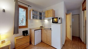 Una cocina compacta con armarios de madera, microondas, lavavajillas y una ventana con cortinas.