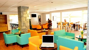 A spacious lobby with teal and yellow seating, a stone pillar, and a laptop on a table.