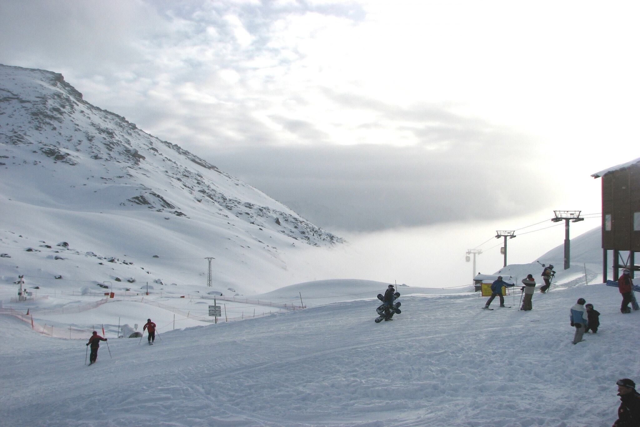 Een besneeuwde piste met skiërs en snowboarders.