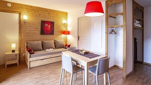 A cozy room with a wooden wall, a dining table with chairs, a red pendant light, a sofa with cushions, and a wardrobe. - Mountain view apartment in Orelle (Orelle)