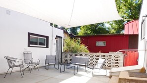A covered patio area with outdoor furniture, including chairs and a table, and a red building in the background. - Entire House * Kid Ready * Yard (Arvada)