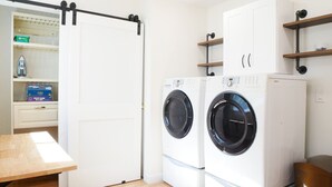 A laundry room with two front-loading washing machines, a wooden table, and a white wardrobe with a sliding door. - Entire House * Kid Ready * Yard (Arvada)