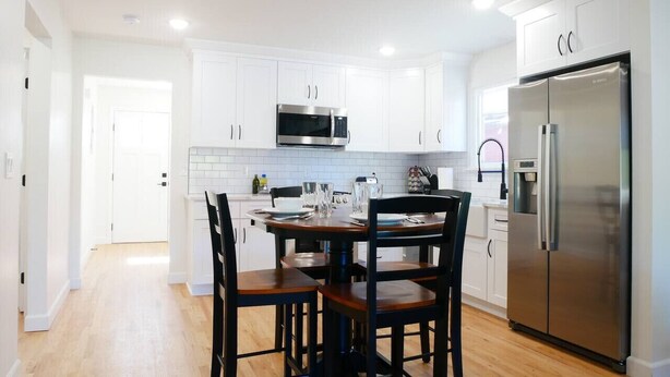 A modern kitchen with white cabinets, a stainless steel refrigerator, and a dining table with chairs. - Entire House * Kid Ready * Yard (Arvada)
