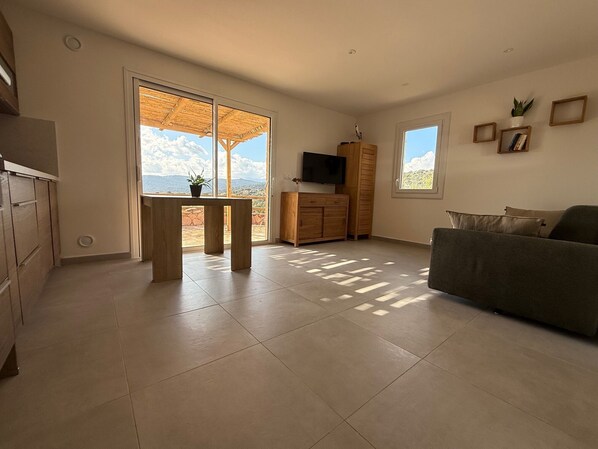 A spacious living room with a large window, a flat-screen TV, a wooden cabinet, and a sofa.