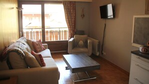 A living room with a sofa, a coffee table, a TV, and a balcony with a view. - Studio in Châtel near Portes du Soleil Ski Area (Châtel)