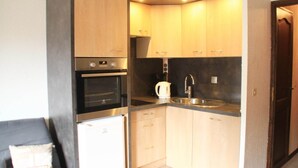 A compact kitchen with wooden cabinets, a built-in oven, a coffee maker, and a sink.