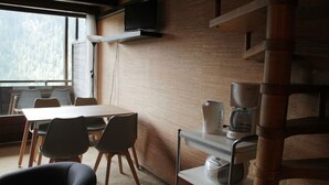 Uma área de refeições com uma mesa, cadeiras, uma máquina de café e uma televisão na parede.