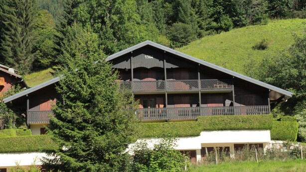 A multi-story chalet with a balcony on the upper floor, surrounded by lush greenery and a hilly landscape. - Apartment for 3 people with balcony (Châtel)