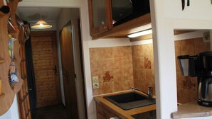 A narrow kitchen with wooden cabinets, a built-in microwave, and a coffee maker. - Apartment for 3 people with balcony (Châtel)