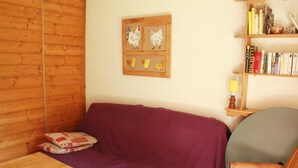 A room with a wooden wall, a purple sofa, a wooden chair, a small table, and a bookshelf with books and a lamp. - Apartment for 3 people with balcony (Châtel)