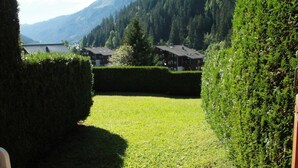 A well-maintained grassy area with neatly trimmed hedges, a building with multiple windows, and a mountainous backdrop. - Apartment for 3 people with balcony (Châtel)