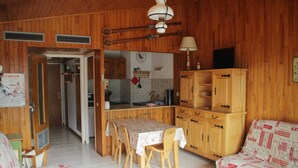 Una habitación con paneles de madera, una mesa de comedor, sillas, un sofá y una kitchenette.