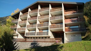 Un hotel de varios pisos con balcones, fachada de piedra y un paisaje montañoso al fondo.