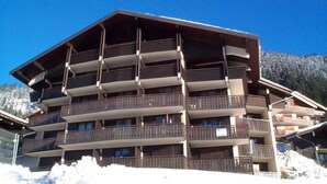 Un hôtel à plusieurs étages doté de balcons, avec une piste de ski en arrière-plan et un ciel bleu dégagé.