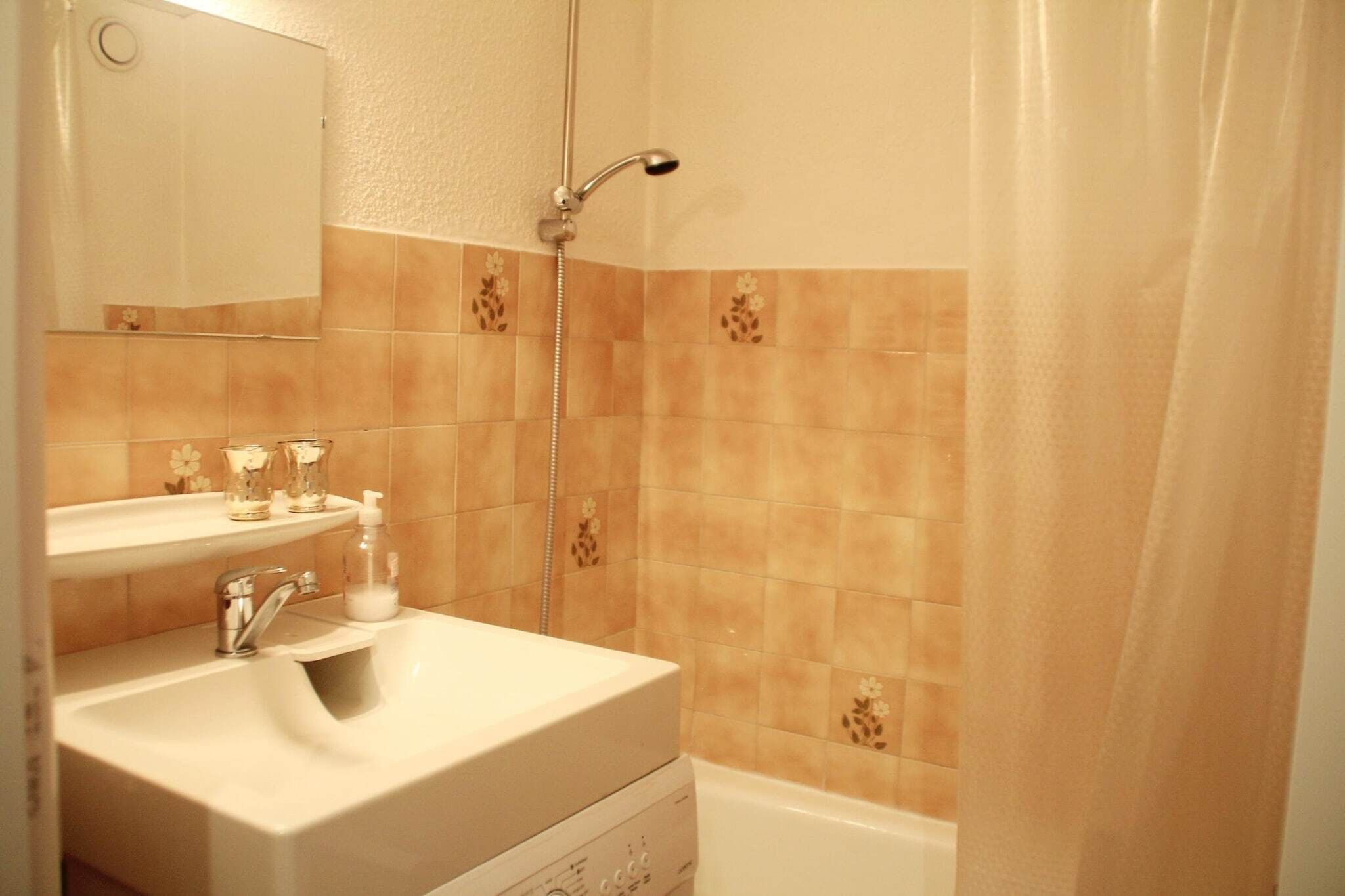 A bathroom with a sink, mirror, shower, and tiled walls.