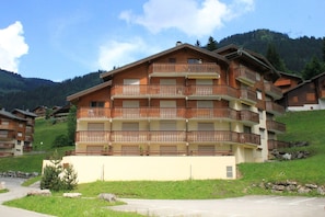 A multi-story wooden building with balconies, set against a mountainous backdrop.
