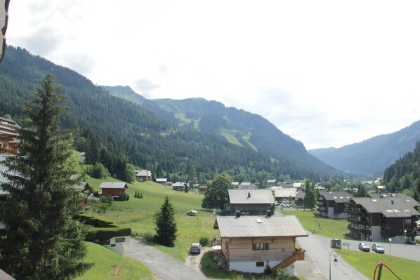 A mountain village with wooden houses, a paved road, and a view of the surrounding hills.