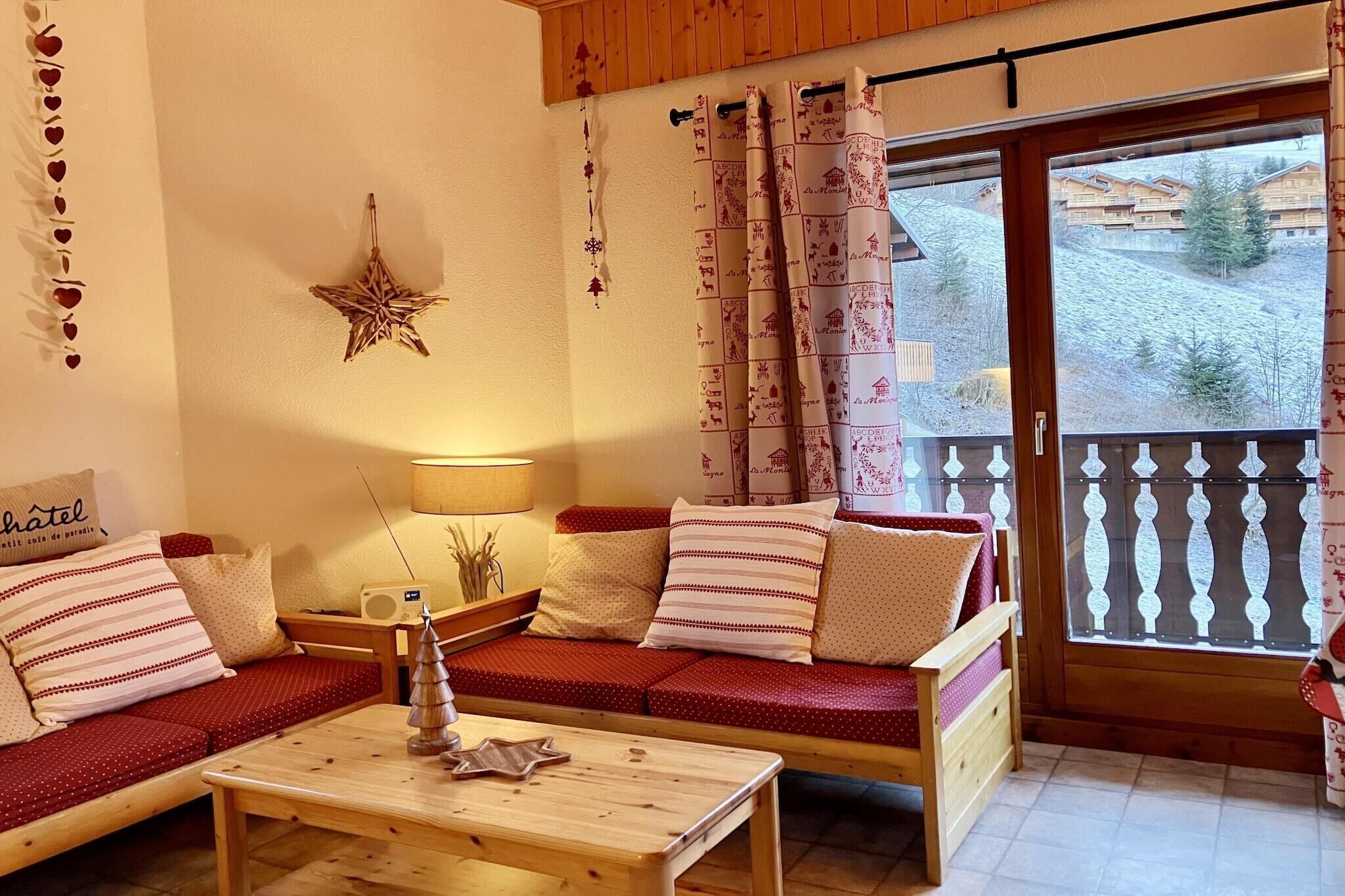 A cozy living room with a wooden sofa, a small table, and a balcony with a view of a ski resort.