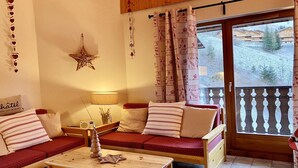 Un salon chaleureux avec un canapé en bois, une petite table et un balcon offrant une vue sur une station de ski.