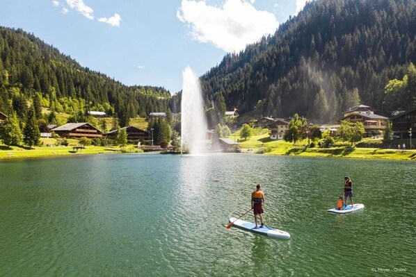 A lake with paddleboards, a fountain, and houses in a mountainous area. - Apartment near centre Chatel with balcony (Châtel)