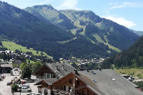 A mountain town with wooden buildings, a road, and a valley.