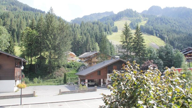 A mountain village with traditional wooden buildings, a parking area, and a view of forested hills. - Apartment for 3 people in Chatel (Châtel)