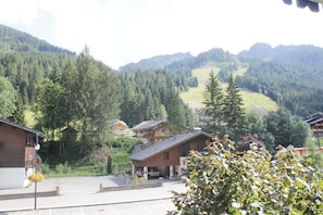 A mountain village with traditional wooden buildings, a parking area, and a view of forested hills.