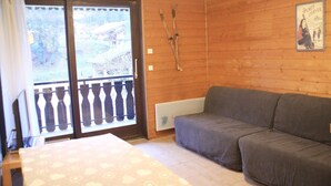 A room with a grey sofa, a window with a view of a forest, and a poster on the wall. - Apartment for 3 people in Chatel (Châtel)